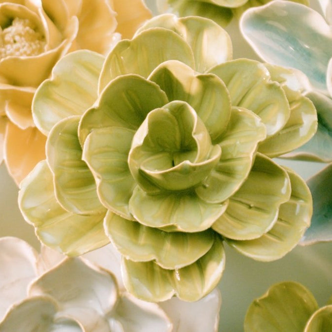 Macro pan across twenty hand-glazed ceramic wall flowers in five palettes — unique wall decor by Chive Studio